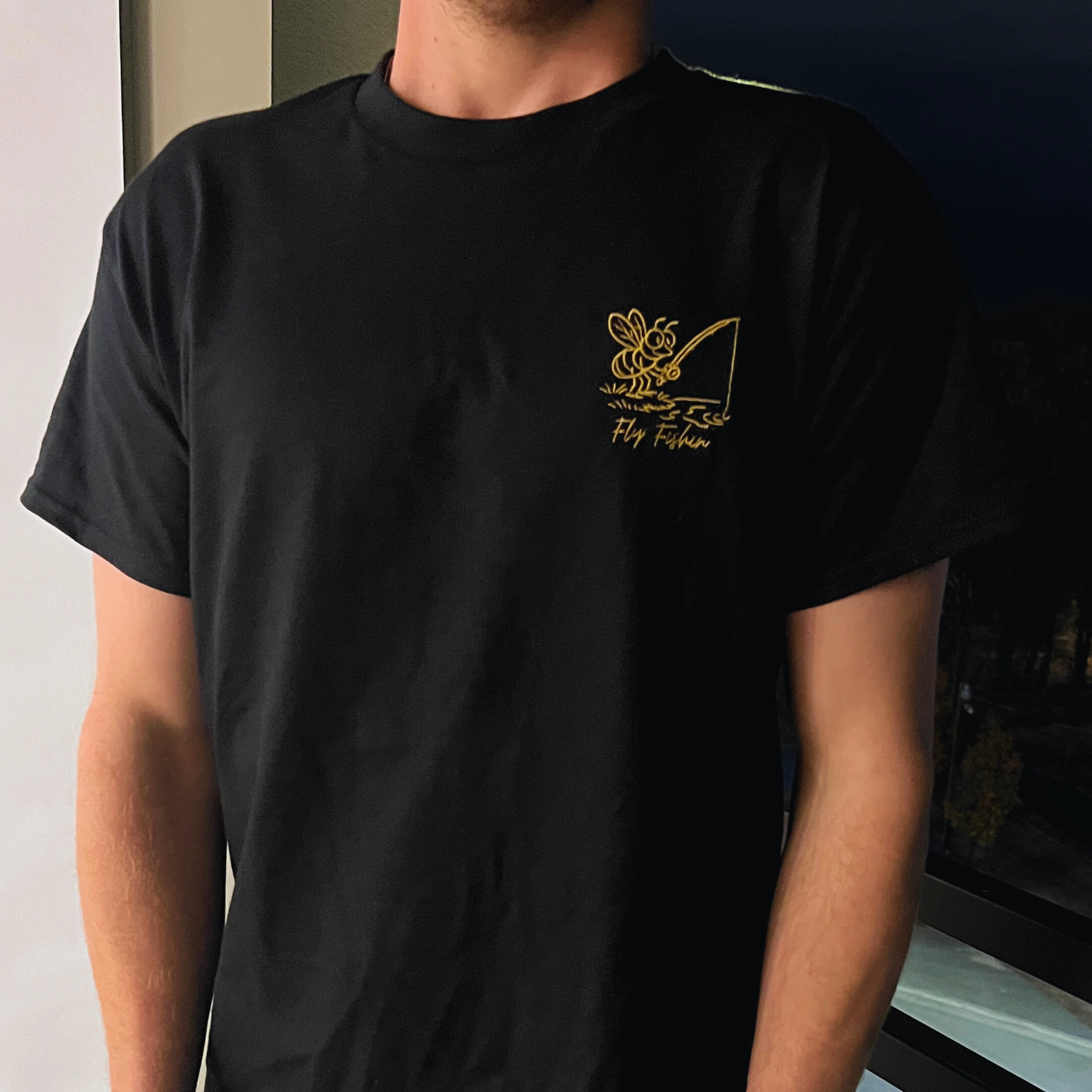 Person wearing a black t-shirt with a gold/yellow logo and text.
